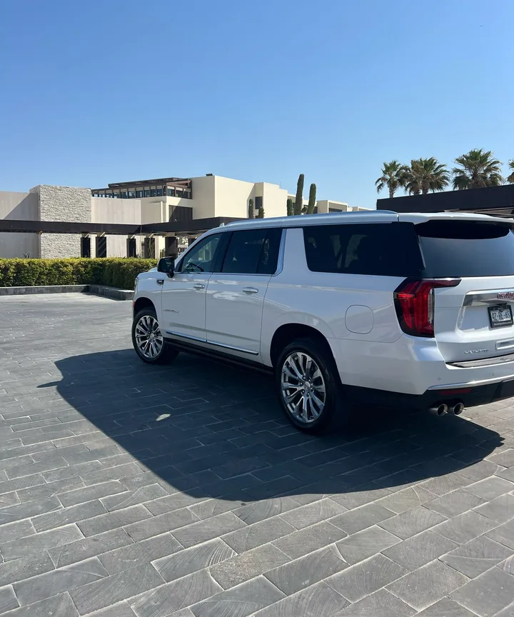 White GMC Yukon Denali for private airport transfers at a resort entrance with cactus and palm trees in Los Cabos